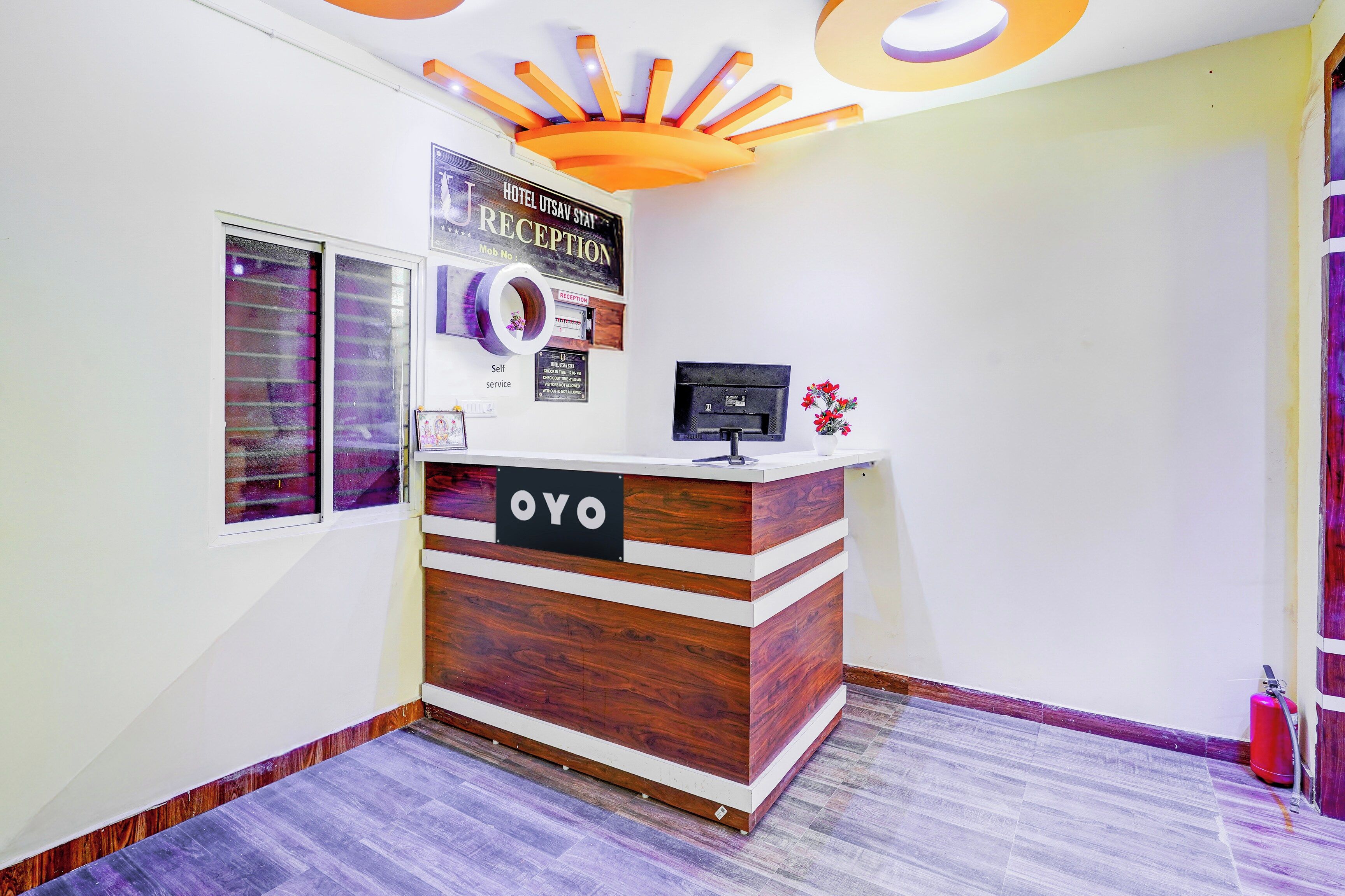 A reception desk with a sign that reads 'OYO' and a reception area with a ceiling design and a fire extinguisher.