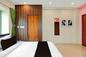 Quarto moderno com uma cama grande, um guarda-roupa de madeira, uma cortina verde e dois painéis decorativos com folhas nas paredes.