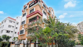 Um edifício de hotel com várias andares, varandas, entrada com portão e vegetação ao redor.