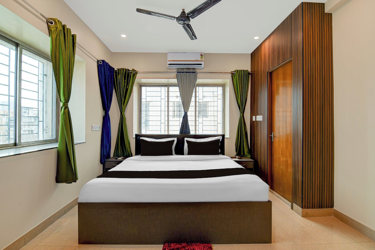 A hotel room with a bed, curtains, a ceiling fan, an air conditioning unit, and a view through the window.