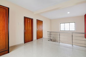 Um quarto espaçoso com piso lustroso, duas portas de madeira, uma janela com persianas e um corrimão de metal.