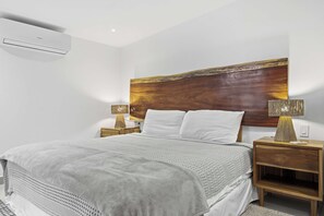 A modern bedroom with a large bed, wooden headboard, two bedside tables with lamps, and an air conditioning unit on the wall. - Private Villa with pool and BBQ (Potrero)