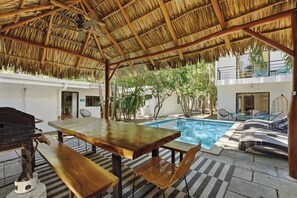 An outdoor pool area with a thatched roof, lounge chairs, and a dining table with chairs. - Private Villa with pool and BBQ (Potrero)