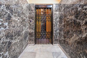 An elevator with a black and yellow gate, marble walls, and a floor with light-colored tiles. - Hotel O MOHAR KUNJHA (Barasat)