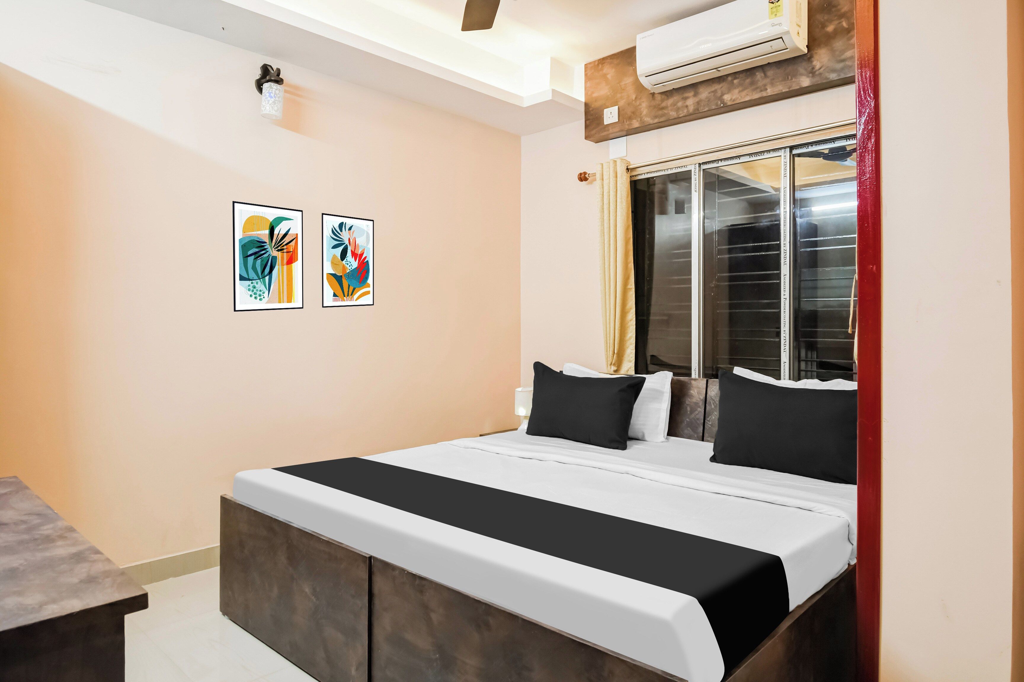 Ein Hotelzimmer mit Bett, Nachttisch, Fenster mit Vorhängen und zwei Wandbildern.