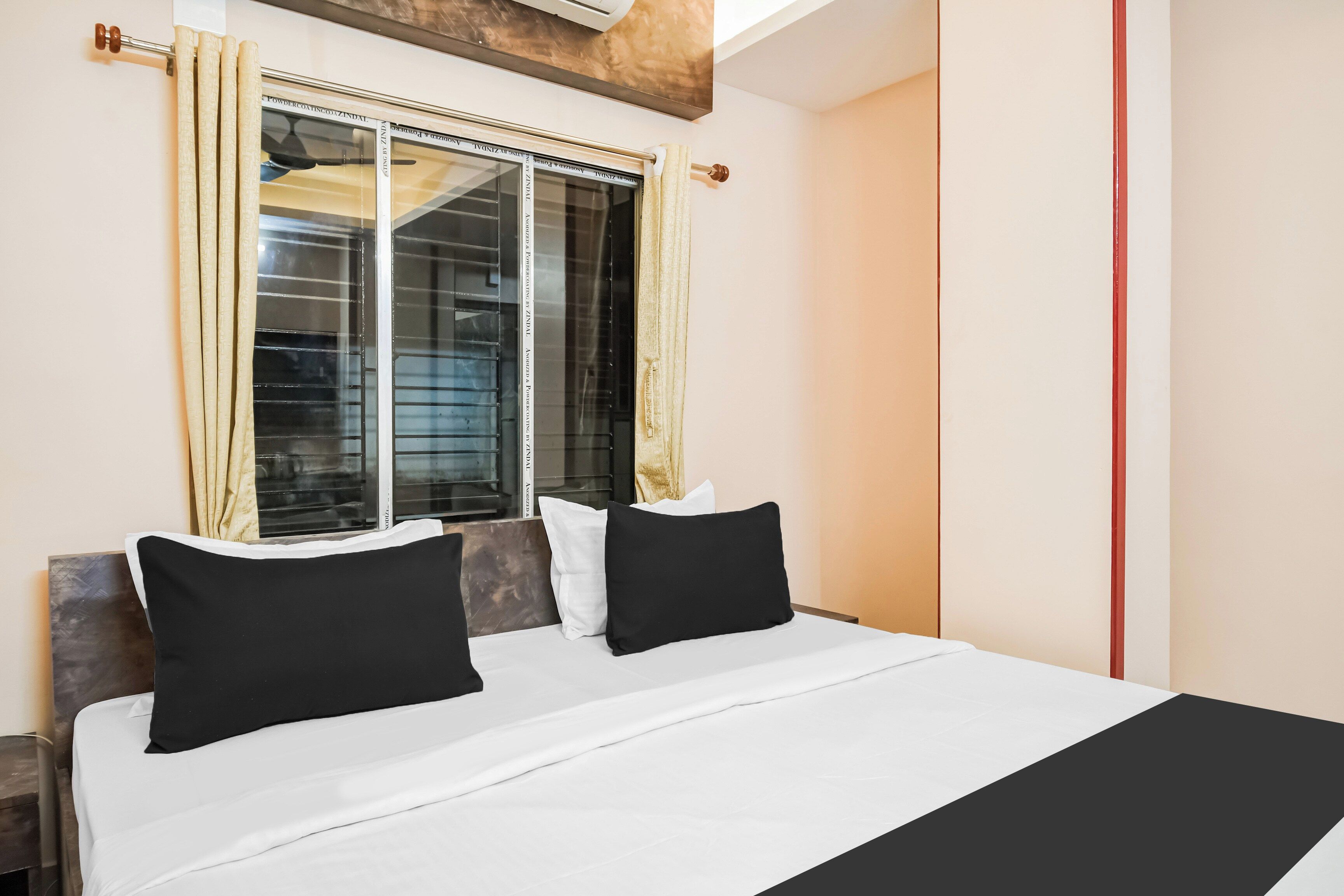 A hotel room with a bed, two pillows, a window with curtains, and a radiator.