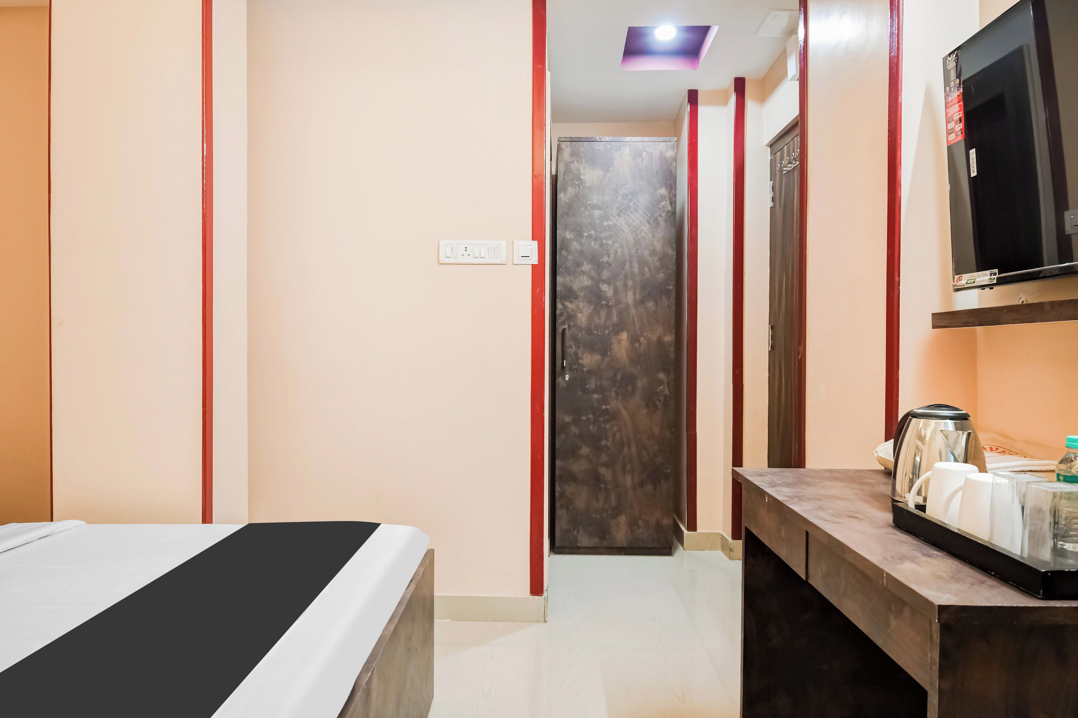 A hotel room with a bed, a TV, a desk with a kettle, and a door leading to another room.