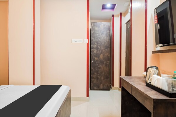 A hotel room with a bed, a TV, a desk with a kettle, and a door leading to another room. - Hotel O MOHAR KUNJHA (Barasat)