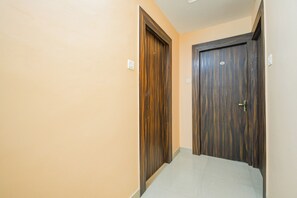 A hallway with two wooden doors, one with a visible number plate, and a light switch on the wall. - Hotel O MOHAR KUNJHA (Barasat)