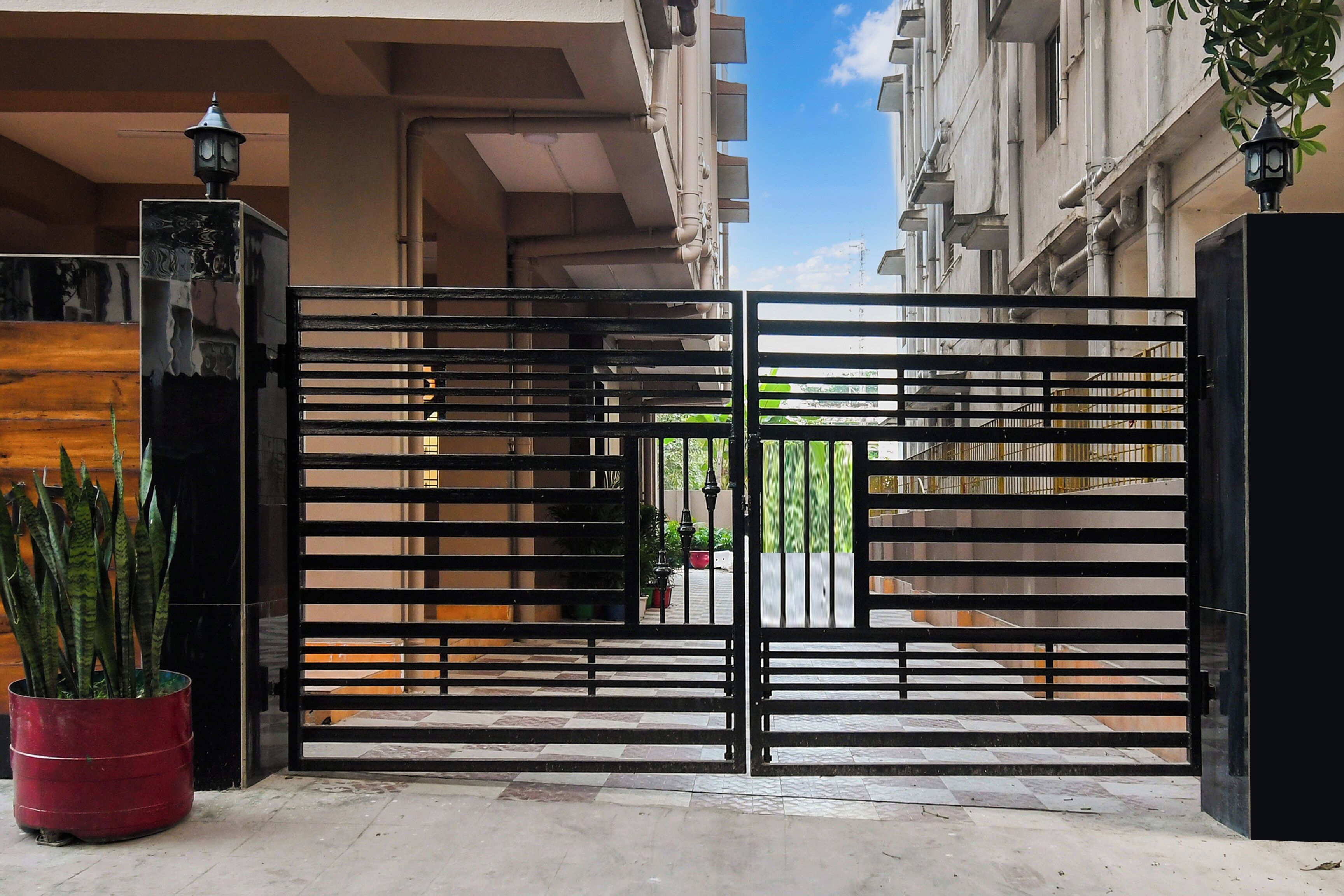 A gated entrance with a metal gate, potted plants, and a building facade in the background.