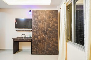 A room with a TV mounted on the wall, a wooden wardrobe, a desk with a kettle, and a window with curtains. - Hotel O MOHAR KUNJHA (Barasat)