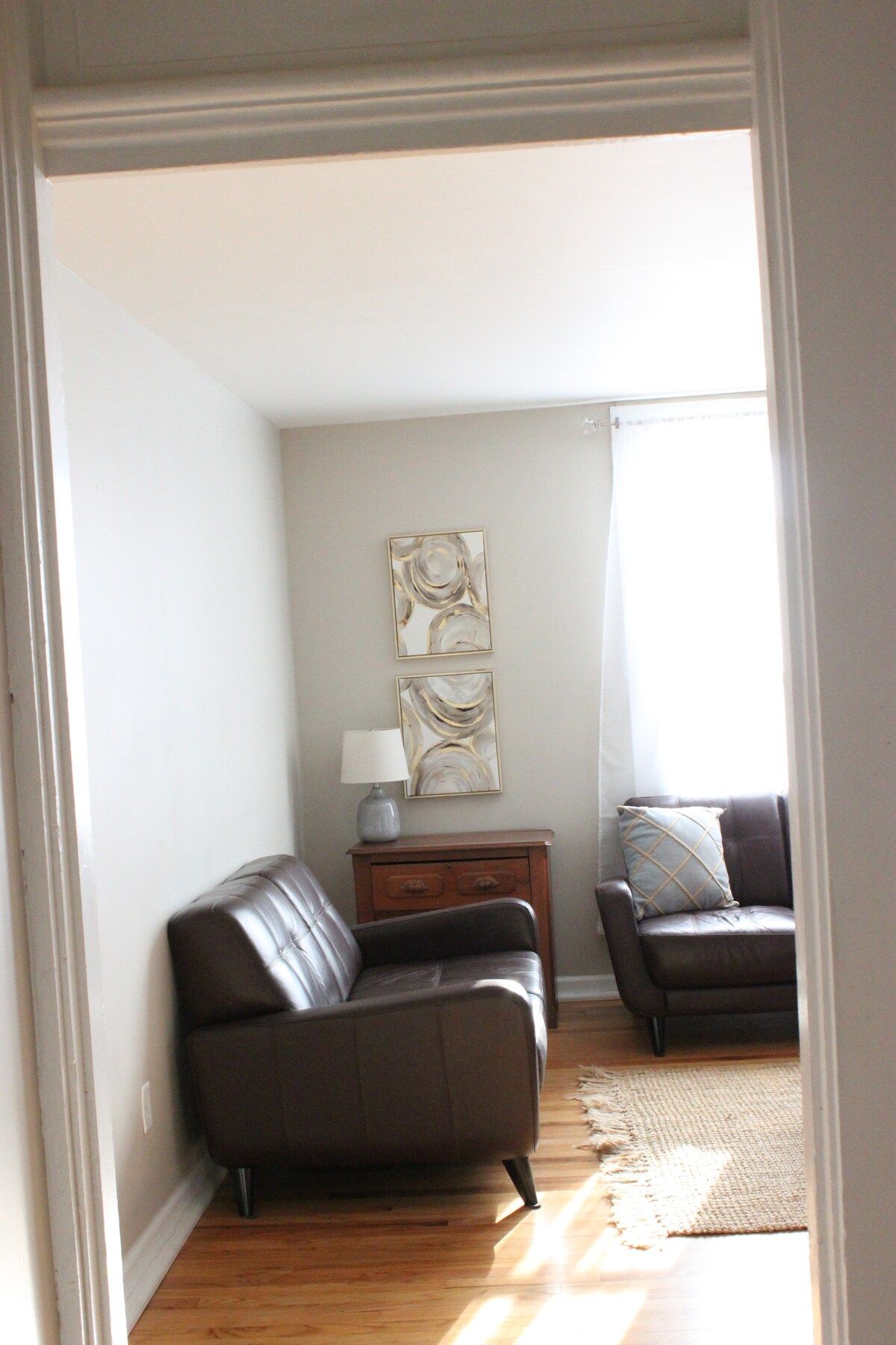 A living room with two leather sofas, a small wooden side table with a lamp, and abstract wall art.