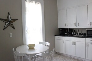 A kitchen with white cabinets, a white table with chairs, a star decoration on the wall, and a window with curtains.