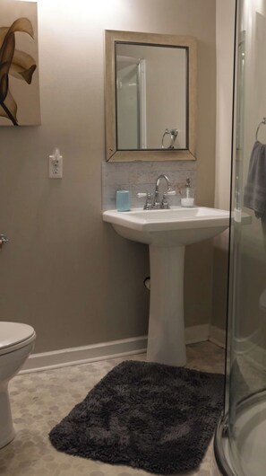Une salle de bain avec un lavabo sur colonne blanc, un miroir au-dessus, un porte-serviettes et un espace douche.
