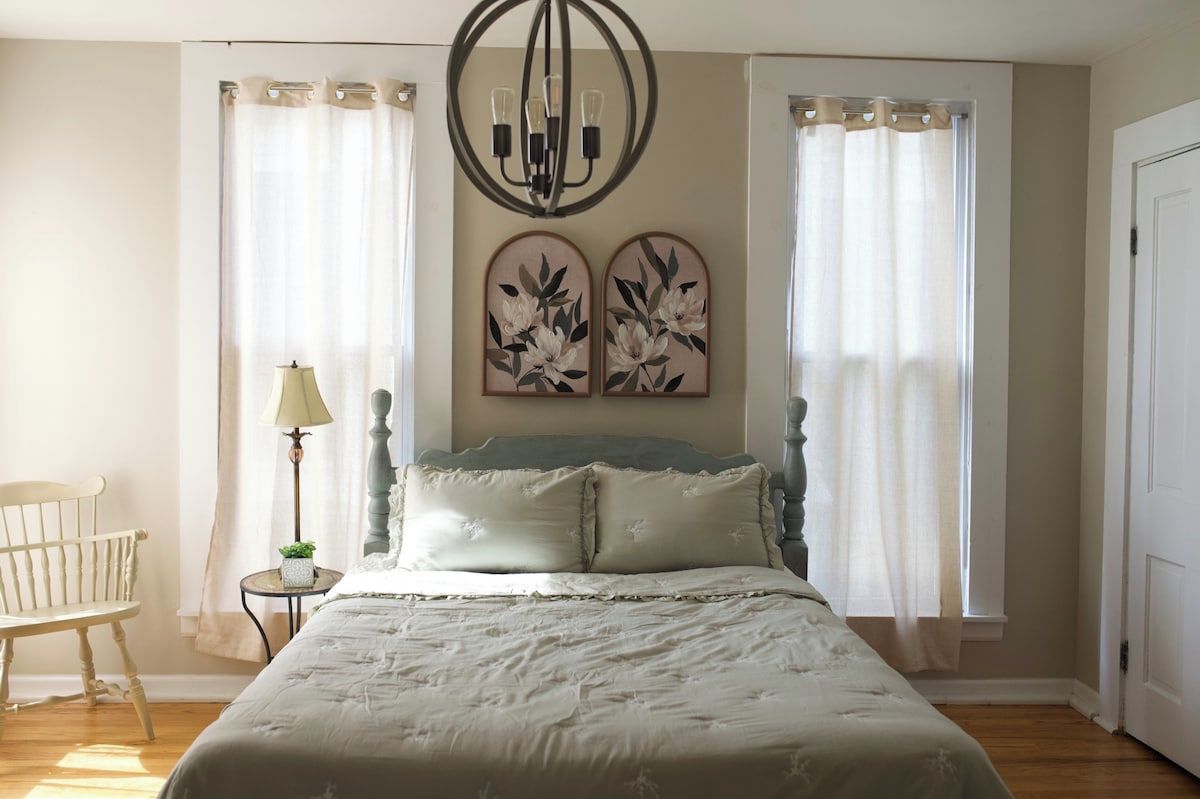 Een slaapkamer met een bed, een stoel, een lamp en twee wanddecoraties.