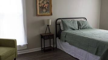 A bedroom with a bed, a nightstand, a lamp, a chair, and a framed picture on the wall.