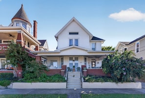 A two-story Victorian-style house with a prominent tower, a front porch, and a staircase leading to the entrance.