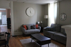 Ein Wohnzimmer mit einem grauen Sofa, einem Couchtisch und einer Wanduhr.