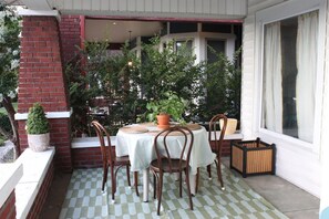 Eine Terrasse mit einem runden Tisch und Stühlen, umgeben von Kübelpflanzen und einer Backsteinmauer.