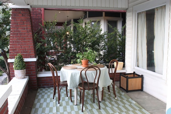 A patio with a round table and chairs, surrounded by potted plants and a brick wall.