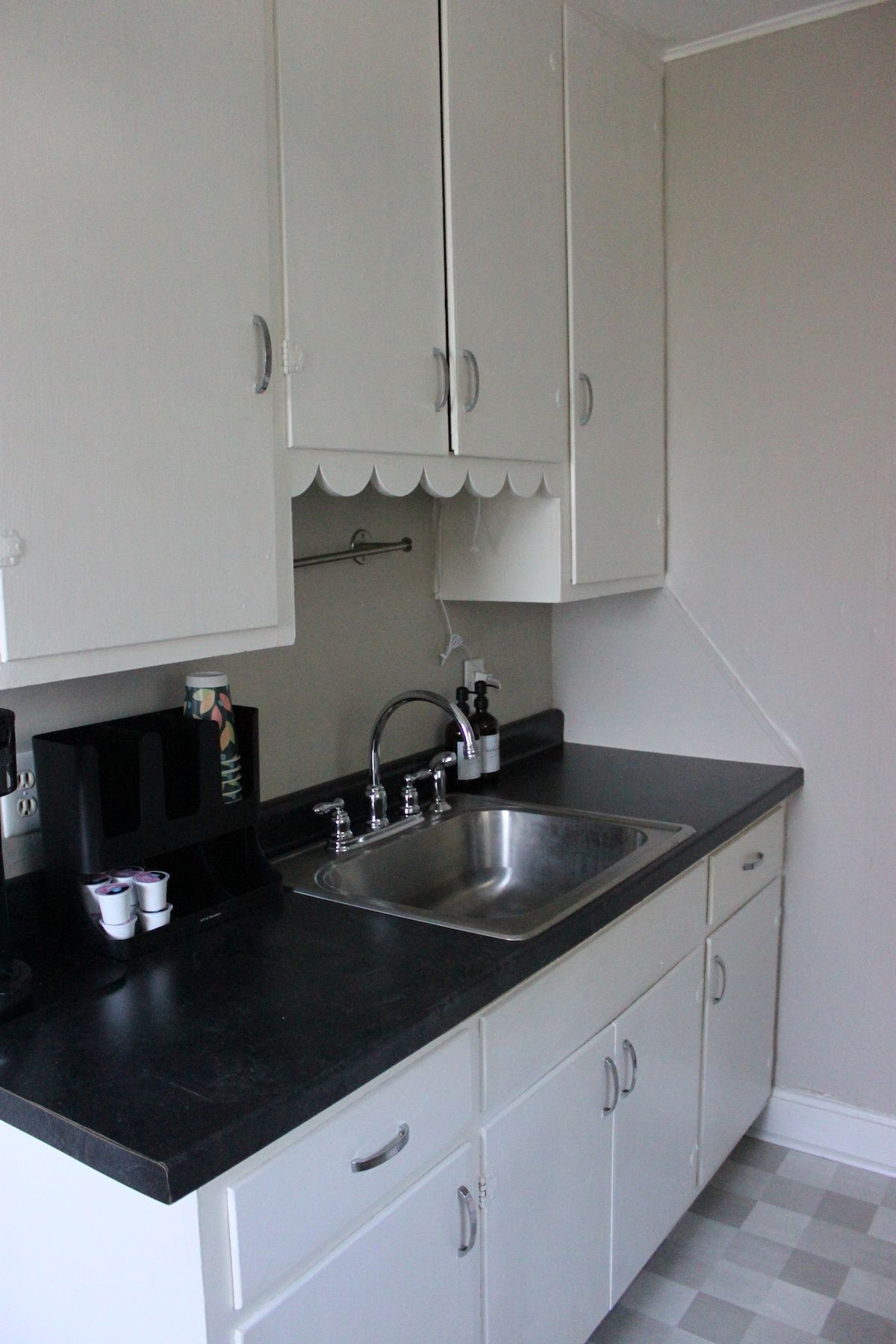 A kitchen with a black countertop, white cabinets, a stainless steel sink, and a small coffee machine.
