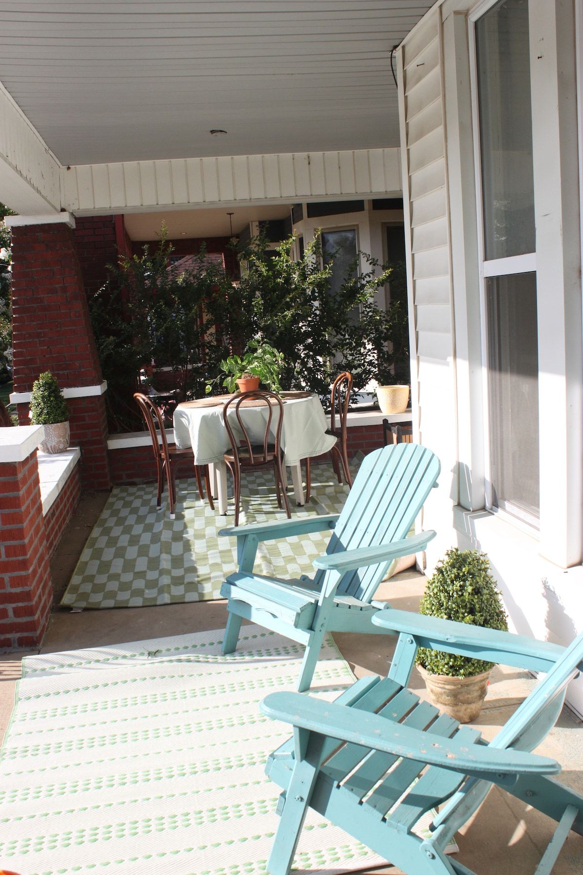 A covered patio with a checkered floor, outdoor furniture, and potted plants.