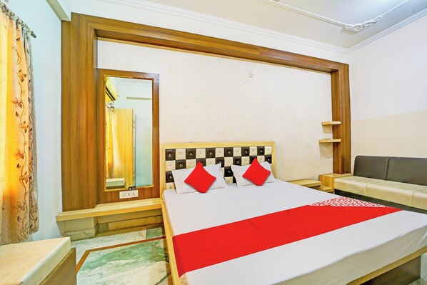 Una habitación de hotel con cama, sofá, mesita de noche, espejo y estante en la pared.