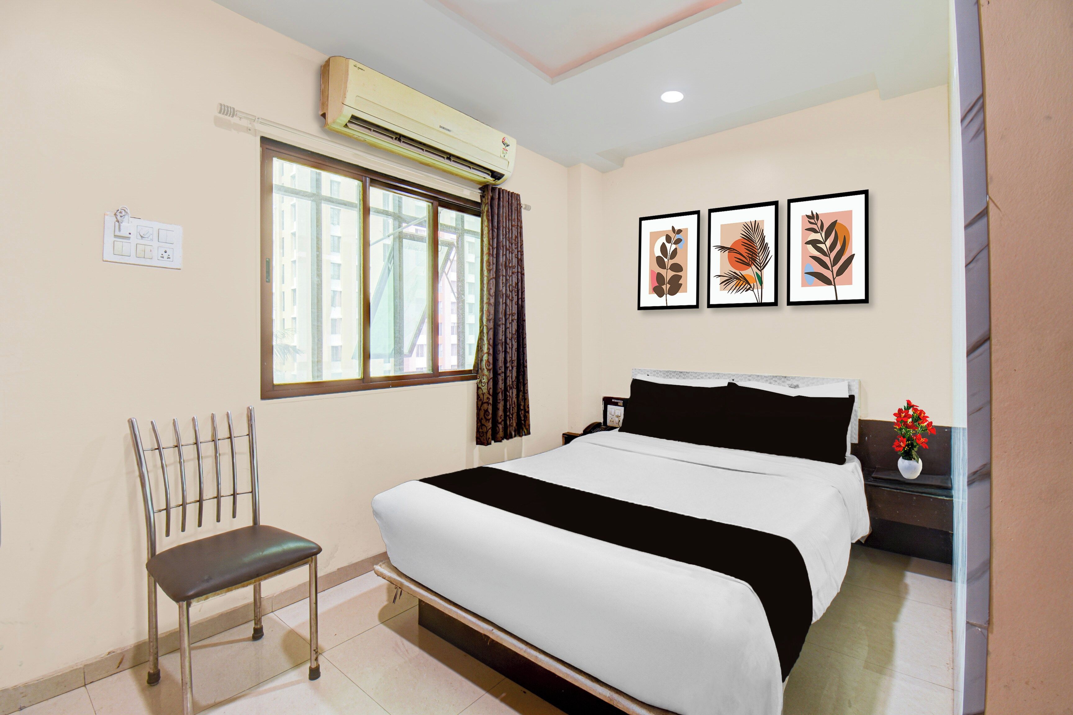 Une chambre d’hôtel avec un lit, une chaise, une fenêtre avec des rideaux et trois œuvres d’art encadrées accrochées au mur.