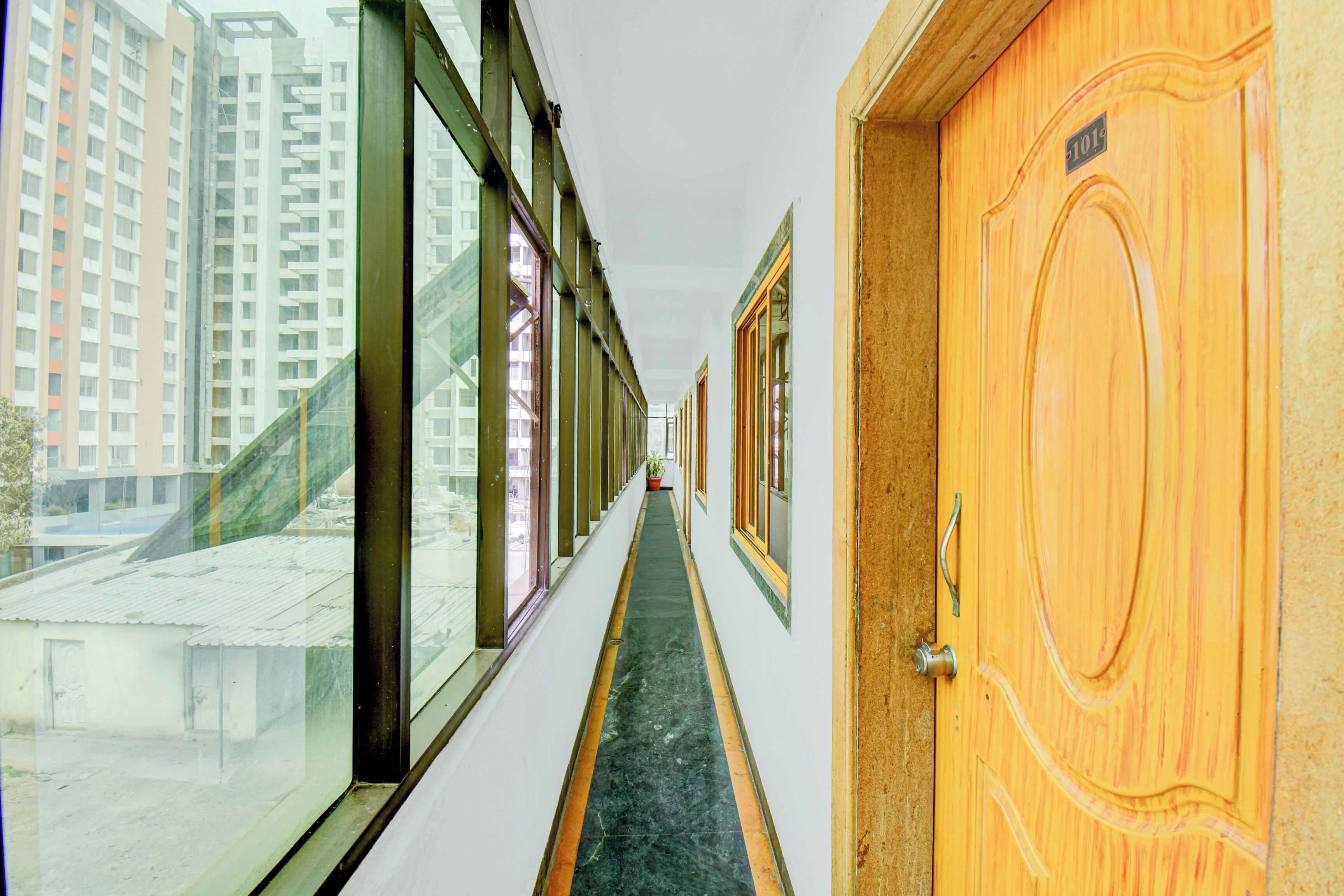 Un couloir avec une porte en bois sur la droite, une fenêtre sur la gauche et une vue sur des immeubles de grande hauteur à l’extérieur.