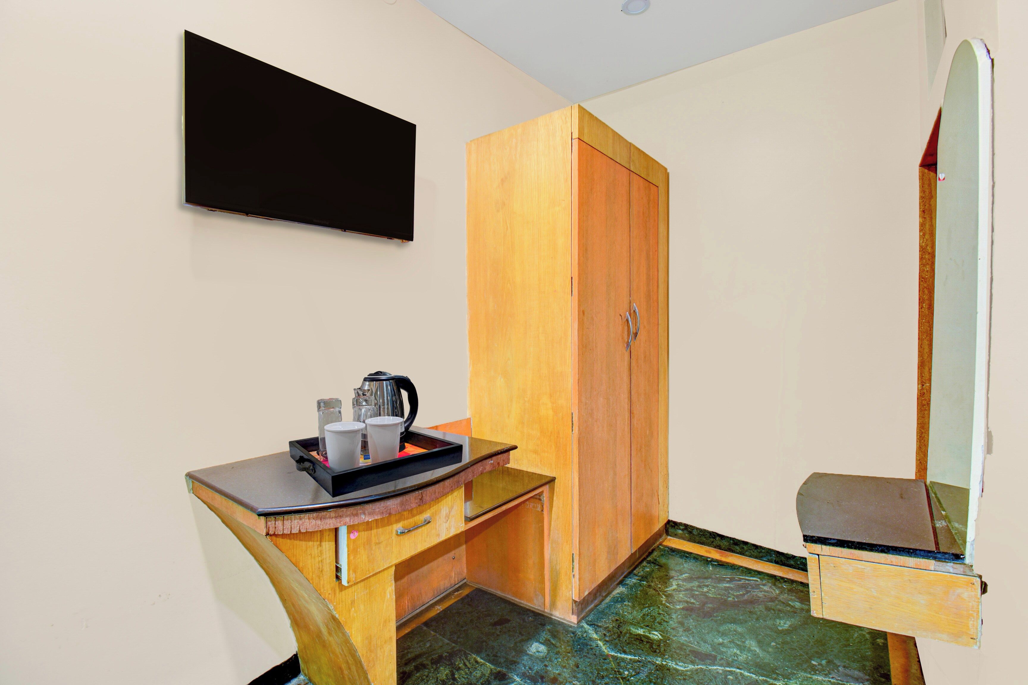 A small room with a wooden cabinet, a flat-screen TV mounted on the wall, a small table with a tray, and a bench.