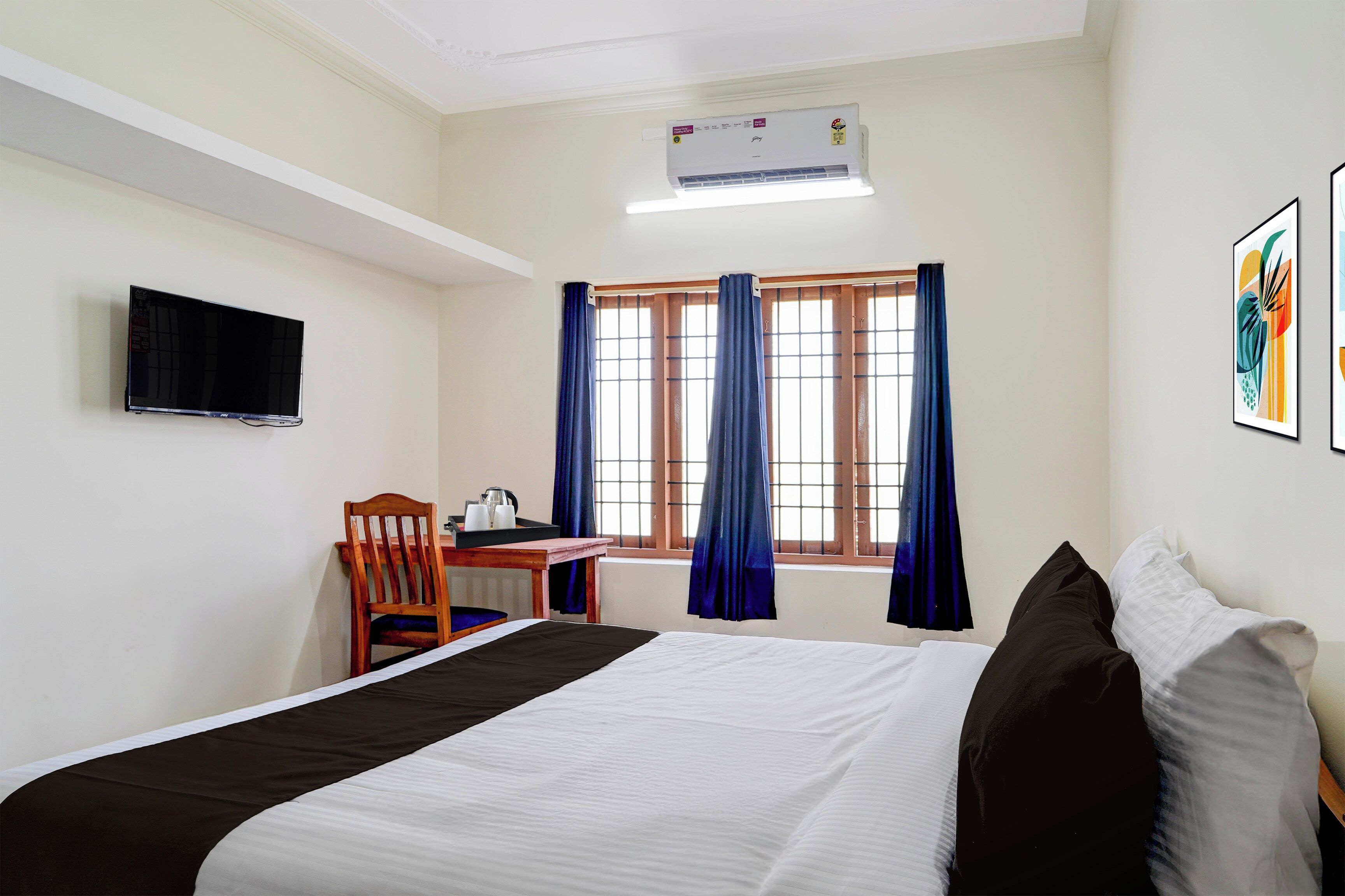 Une chambre d’hôtel avec un lit, un bureau et une chaise, une télévision et une fenêtre avec des rideaux.