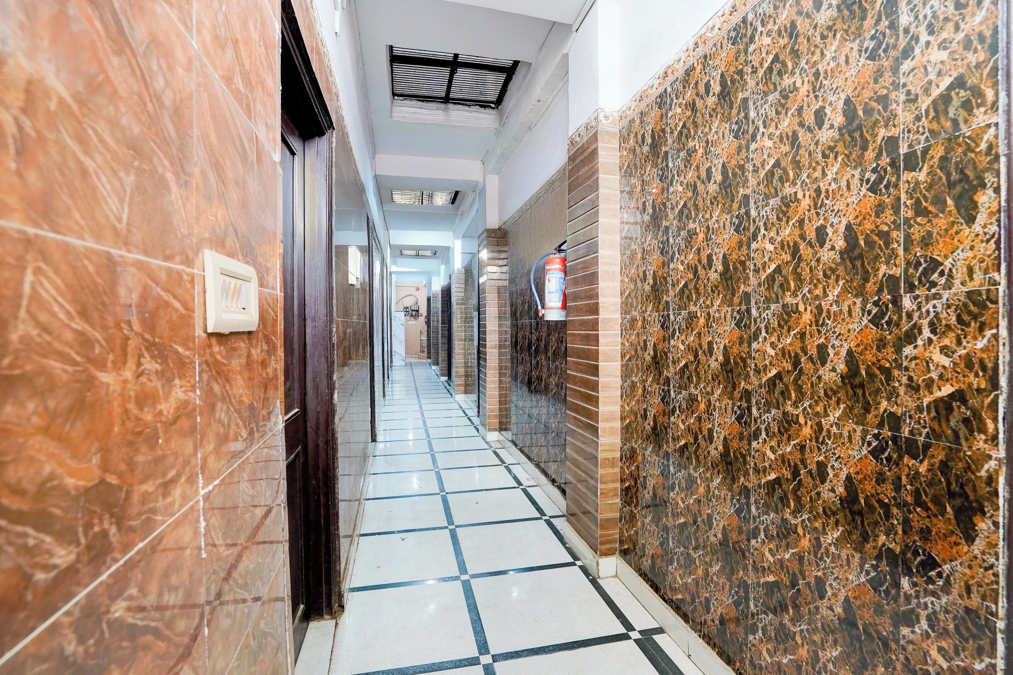 A corridor with tiled flooring, a fire extinguisher mounted on the wall, and a ceiling vent.