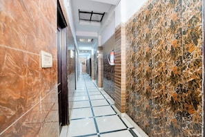 A corridor with tiled flooring, a fire extinguisher mounted on the wall, and a ceiling vent. - Collection O Hindon Airport Ghaziabad (Ghaziabad)