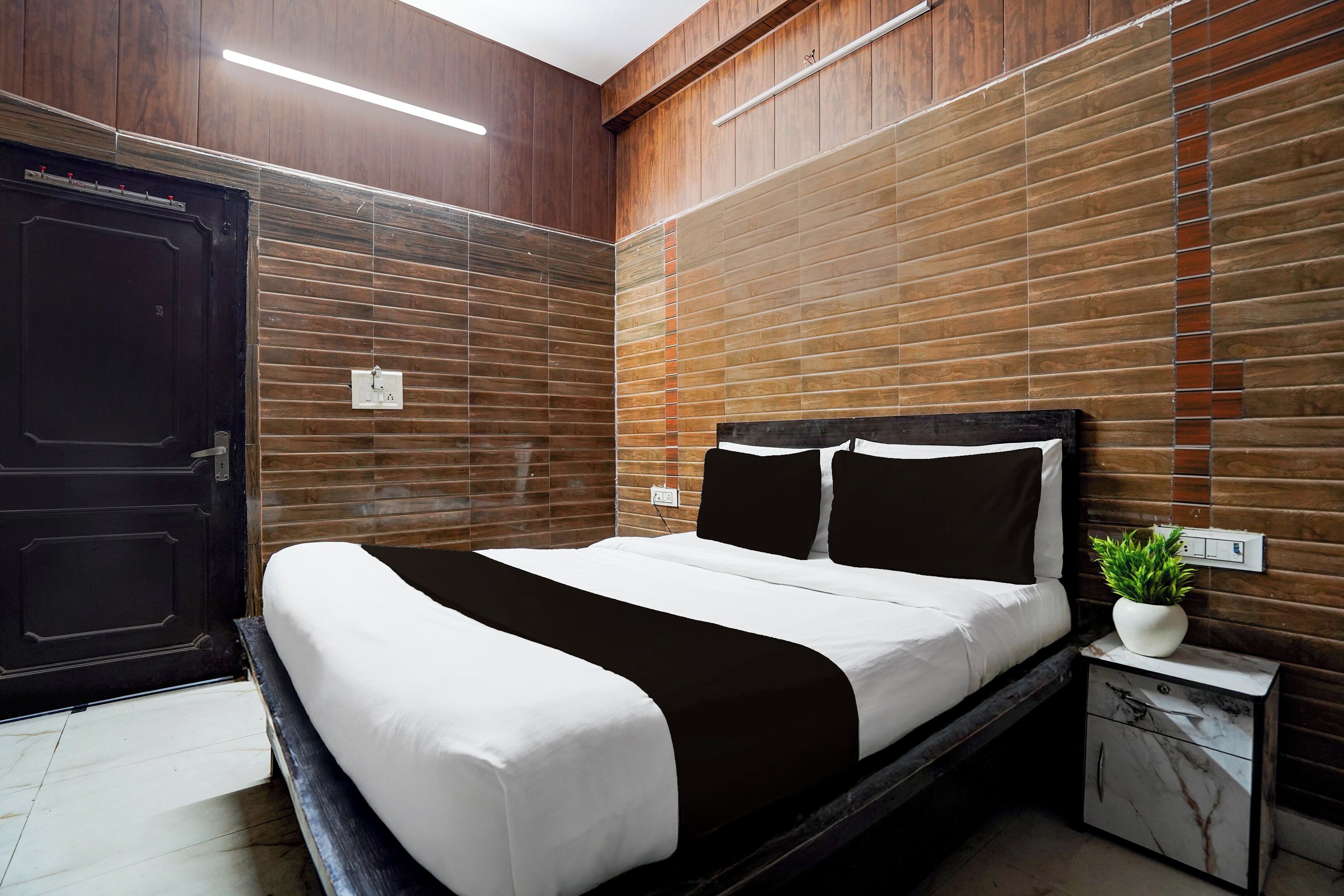 A modern bedroom with a bed, a nightstand, a potted plant, and a wooden wall panel.