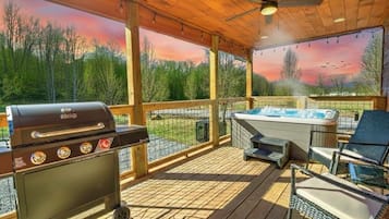 A covered outdoor area with a barbecue grill, a hot tub, and lounge chairs.