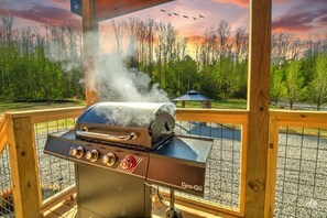 A barbecue grill with a digital display, surrounded by a wooden deck and a view of trees and a gazebo. - Peaceful Cosby Retreat - Hot Tub, Grill, and More! (Cosby)