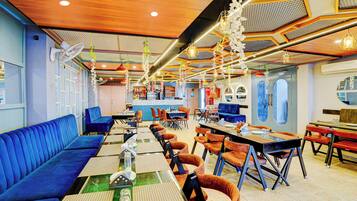 A restaurant with blue seating, tables with place settings, hanging floral decorations, and a patterned ceiling.