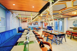 A restaurant with blue seating, tables with place settings, hanging floral decorations, and a patterned ceiling. - Collection O Kotdwar Railway Junction (Kotdwāra)