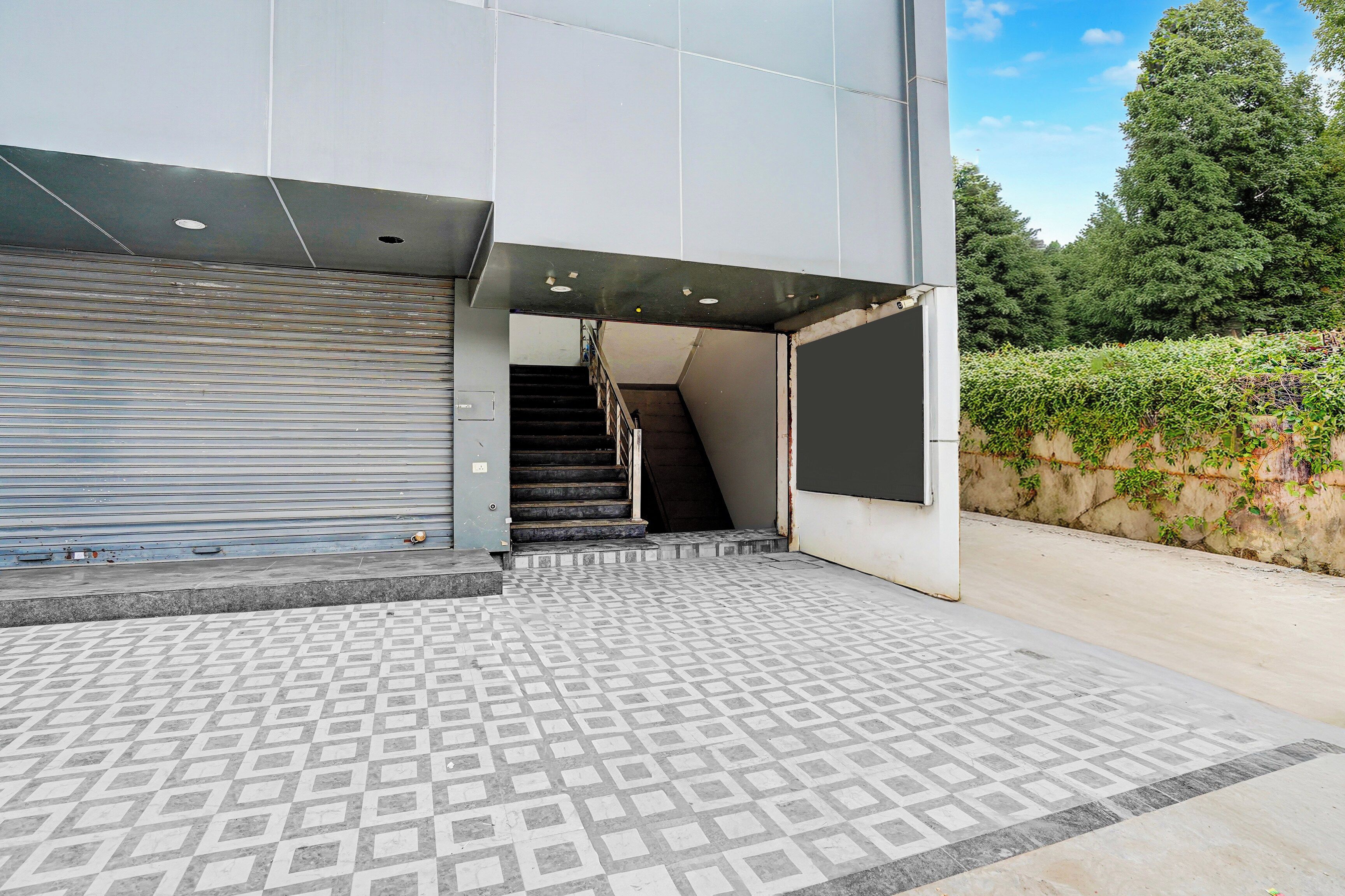 Entrada de un edificio con un toldo metálico enrollable, una escalera que da al interior y un suelo de baldosas con diseño.