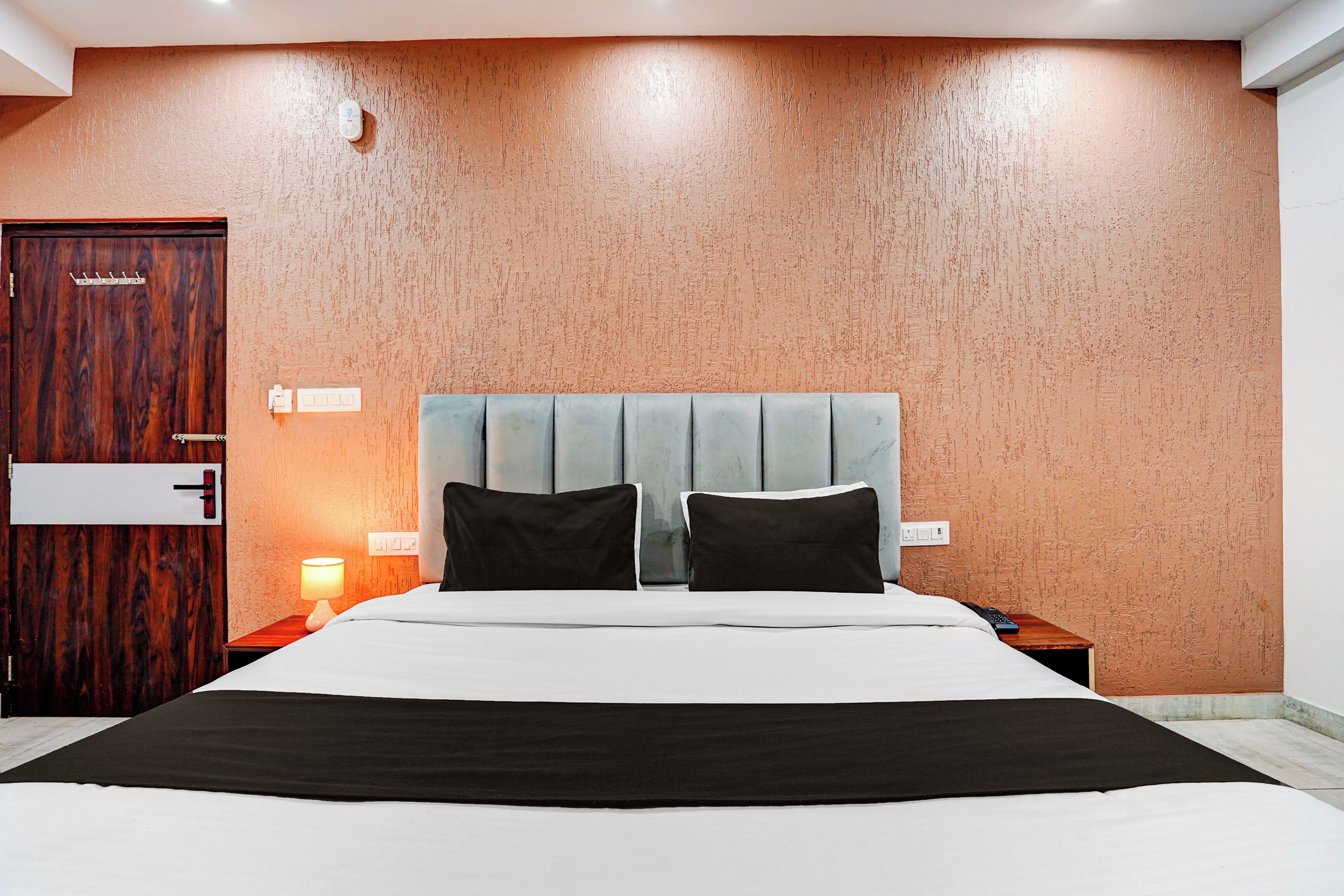 Habitación de hotel con una cama grande, dos mesitas de noche, un armario de madera y una pared con textura.