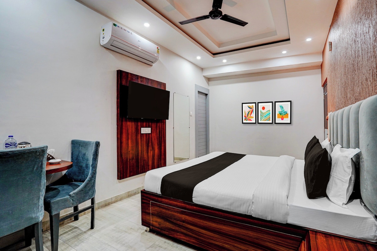 A hotel room with a bed, a desk, a chair, a flat-screen TV, and artwork on the wall.
