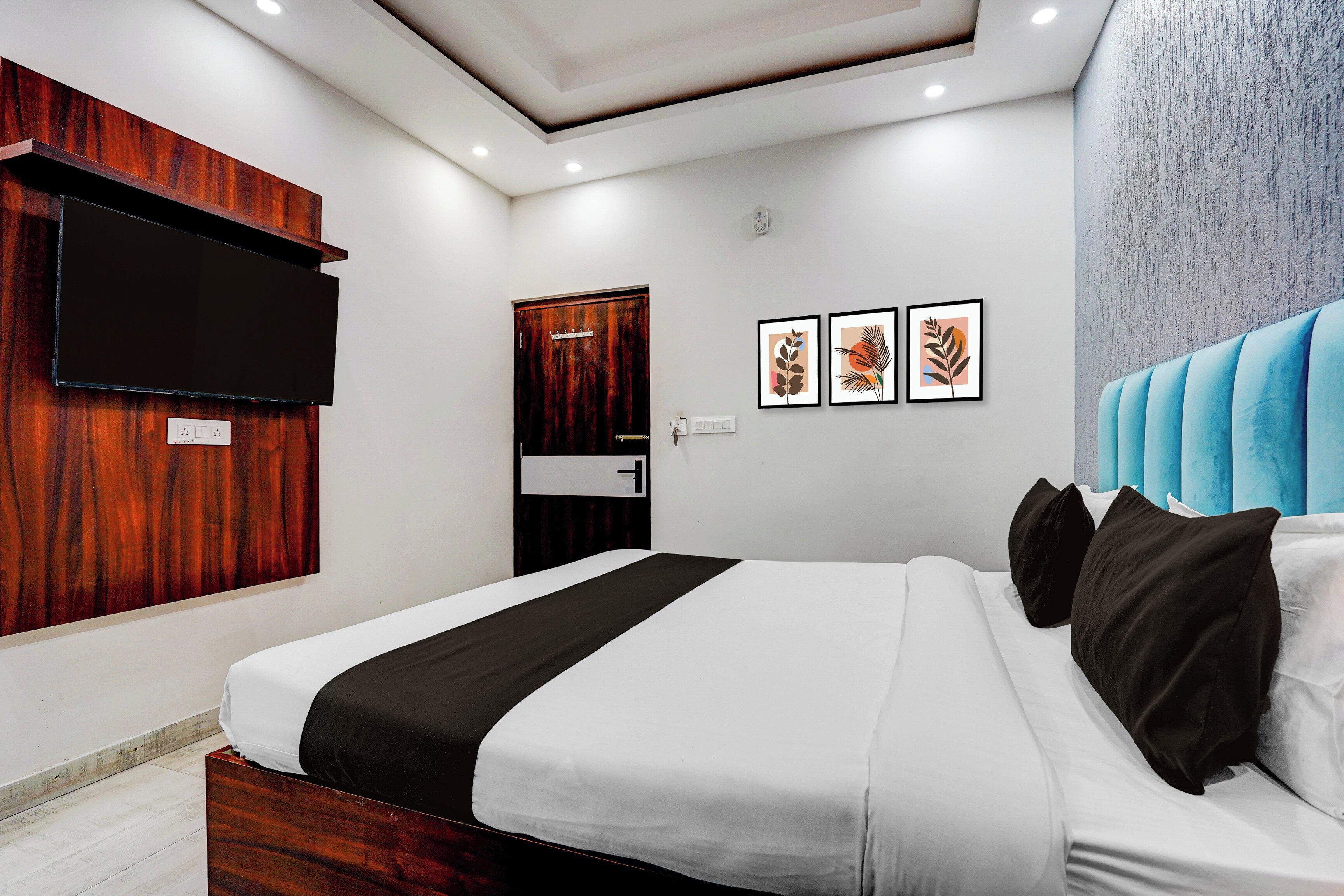 Un dormitorio moderno con una cama grande, un televisor de pantalla plana montado en un panel de madera y tres obras de arte enmarcadas en la pared.