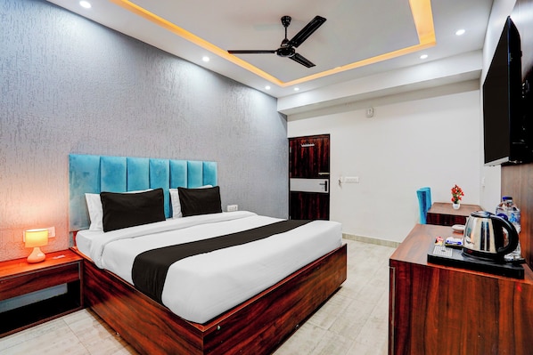 A modern hotel room with a bed, bedside table, nightstand, and a desk with a kettle.