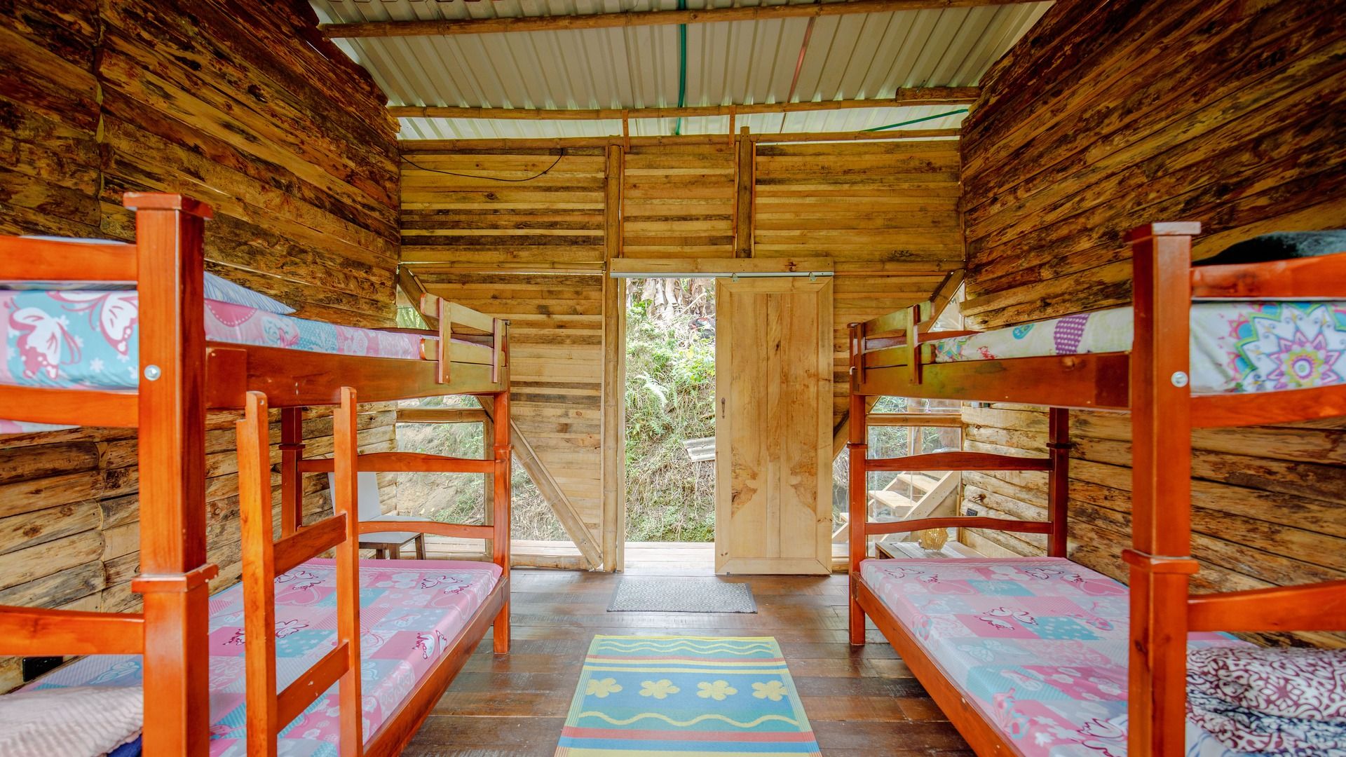 A wooden cabin with bunk beds, a door leading outside, and a patterned rug on the floor.