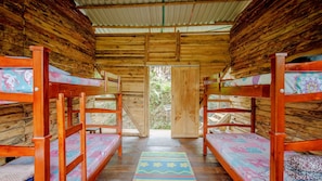 A wooden cabin with bunk beds, a door leading outside, and a patterned rug on the floor. - Reserva Colina de Cristal (Caldas)
