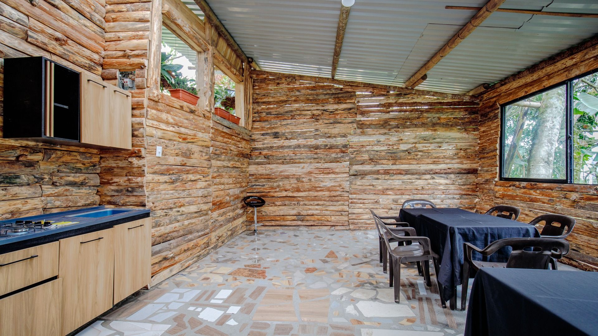 A rustic cabin with a stone wall interior, a dining area with a table and chairs, and a kitchen with wooden cabinets and a gas stove.