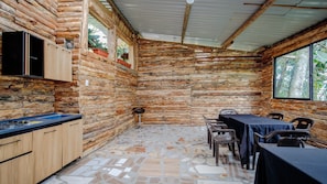 A rustic cabin with a stone wall interior, a dining area with a table and chairs, and a kitchen with wooden cabinets and a gas stove. - Reserva Colina de Cristal (Caldas)