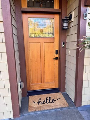 A wooden front door with a glass panel, a doormat with 'hello' written on it, and a wall-mounted light fixture. - The Oakway - Close to UO Campus + Autzen + Golf! (Eugene)