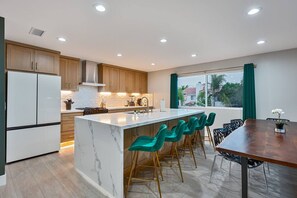 Una cuina moderna amb una illa de marbre, armaris de fusta i una zona de bar amb cadires verdes.