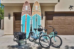 Two surfboards, a bicycle, and a cart with a bag in front of a building with a garage door. - Modern 3BR | Walk to Bay • Pet-Friendly • Parking (San Diego)